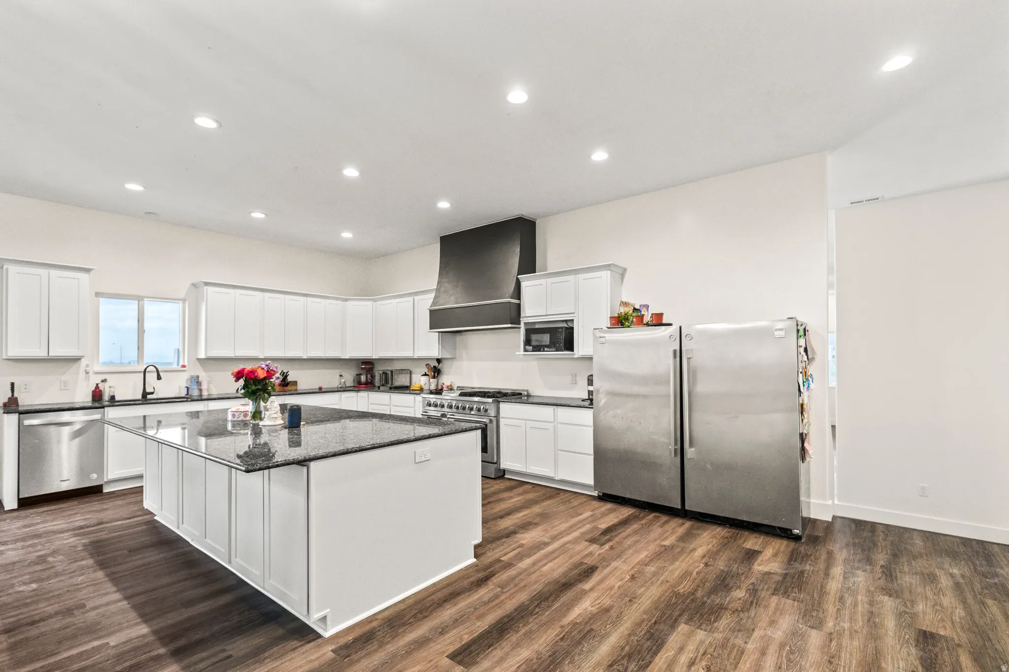 Spacious kitchen featuring an expansive center island with dark countertops, white cabinetry, wood-finish flooring, and stainless steel appliances