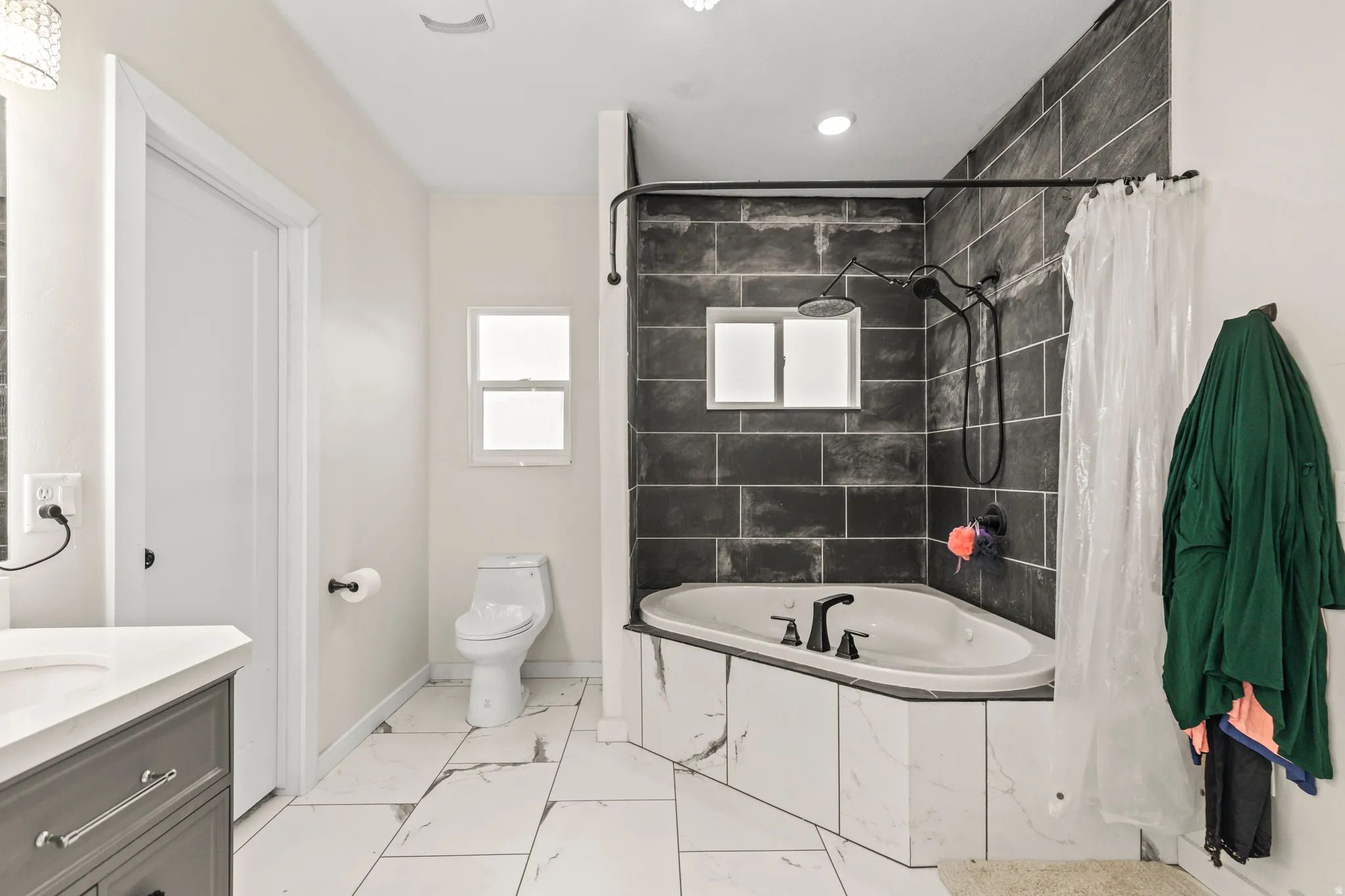 Corner jetted tub with black fixtures, walk-in shower with dark tile surround, light-colored walls, white rectangular window, and white flooring
