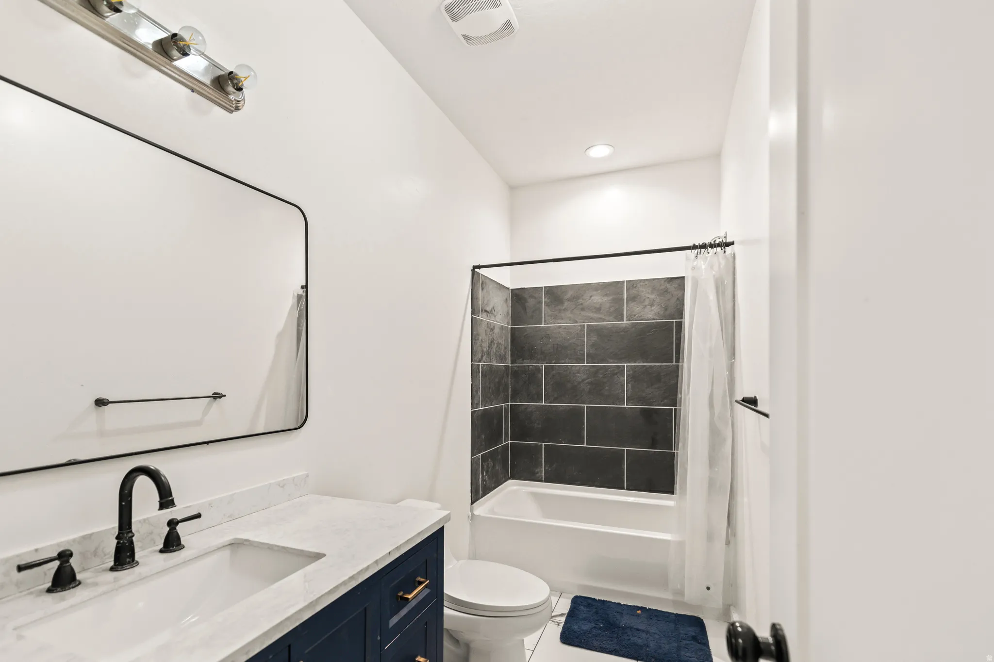 White vanity with a white countertop and matte black fixtures, rectangular mirror, recessed lighting, and a bathtub with subway tile surround