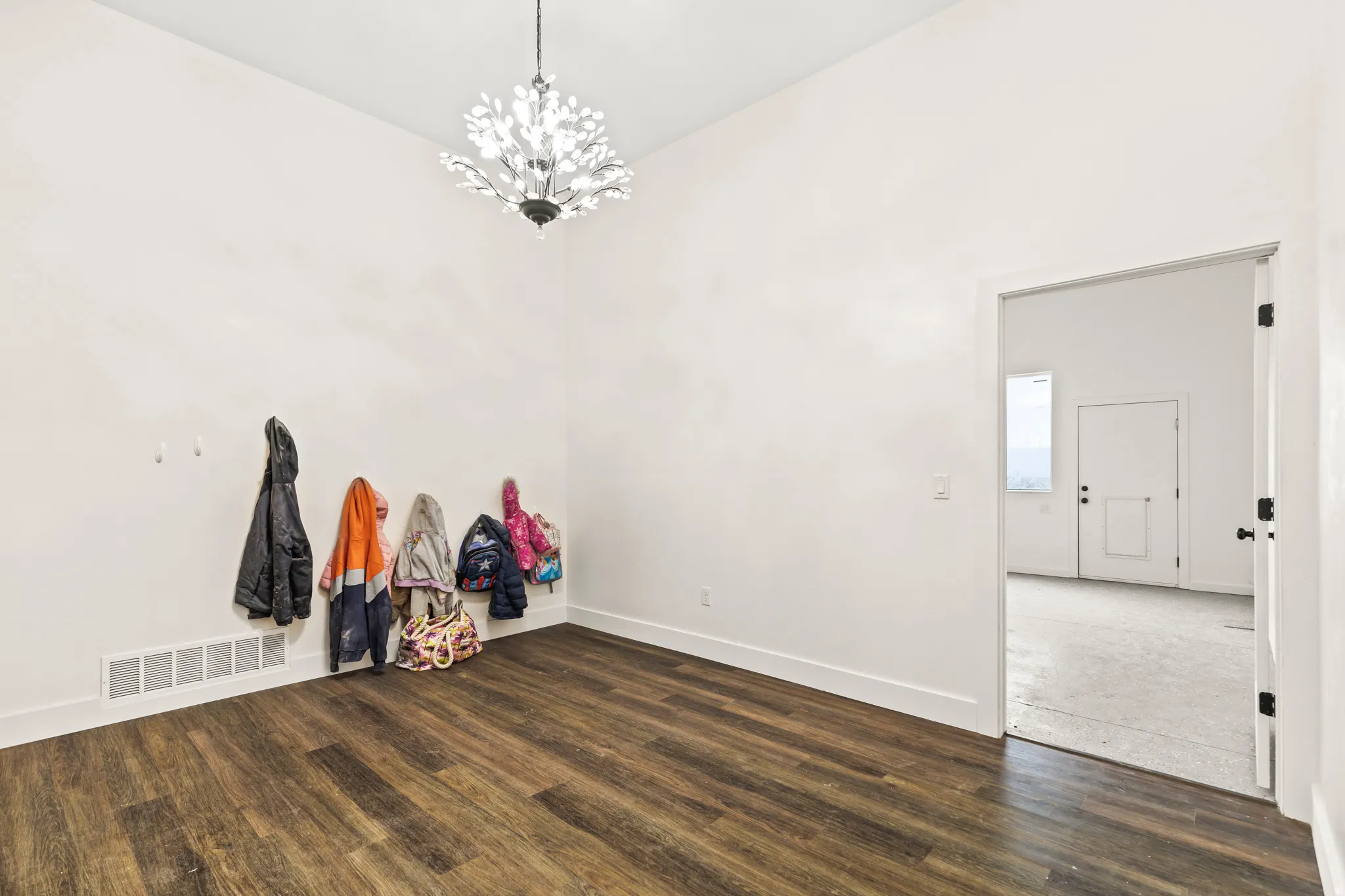 Vaulted ceiling with an ornate chandelier, wood-finish flooring, and white walls