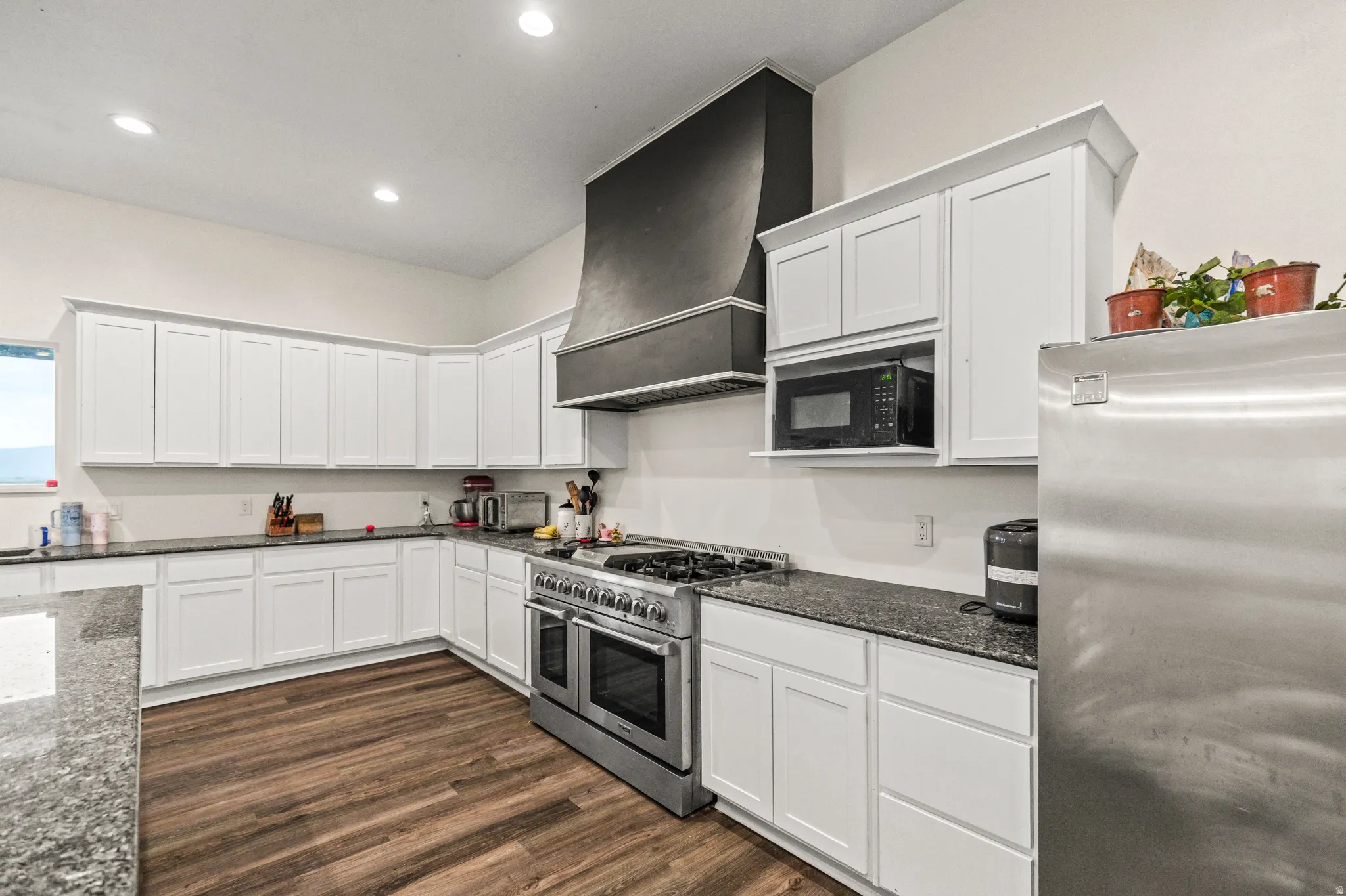 Extensive white cabinetry, dark speckled countertops, stainless steel range with overhead hood, integrated microwave, and wood-finish flooring