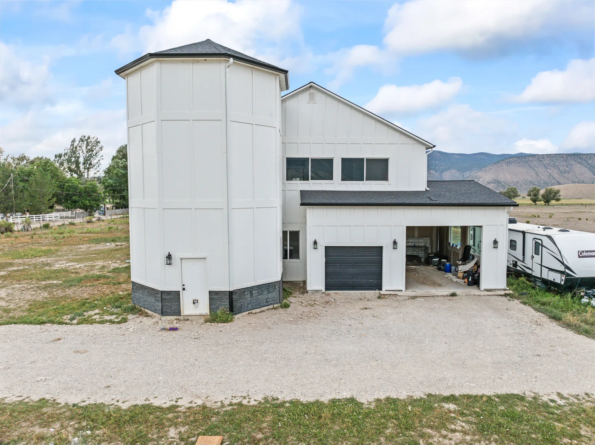 Contemporary farmhouse exterior featuring a silo-style tower, attached garage, and mountain backdrop