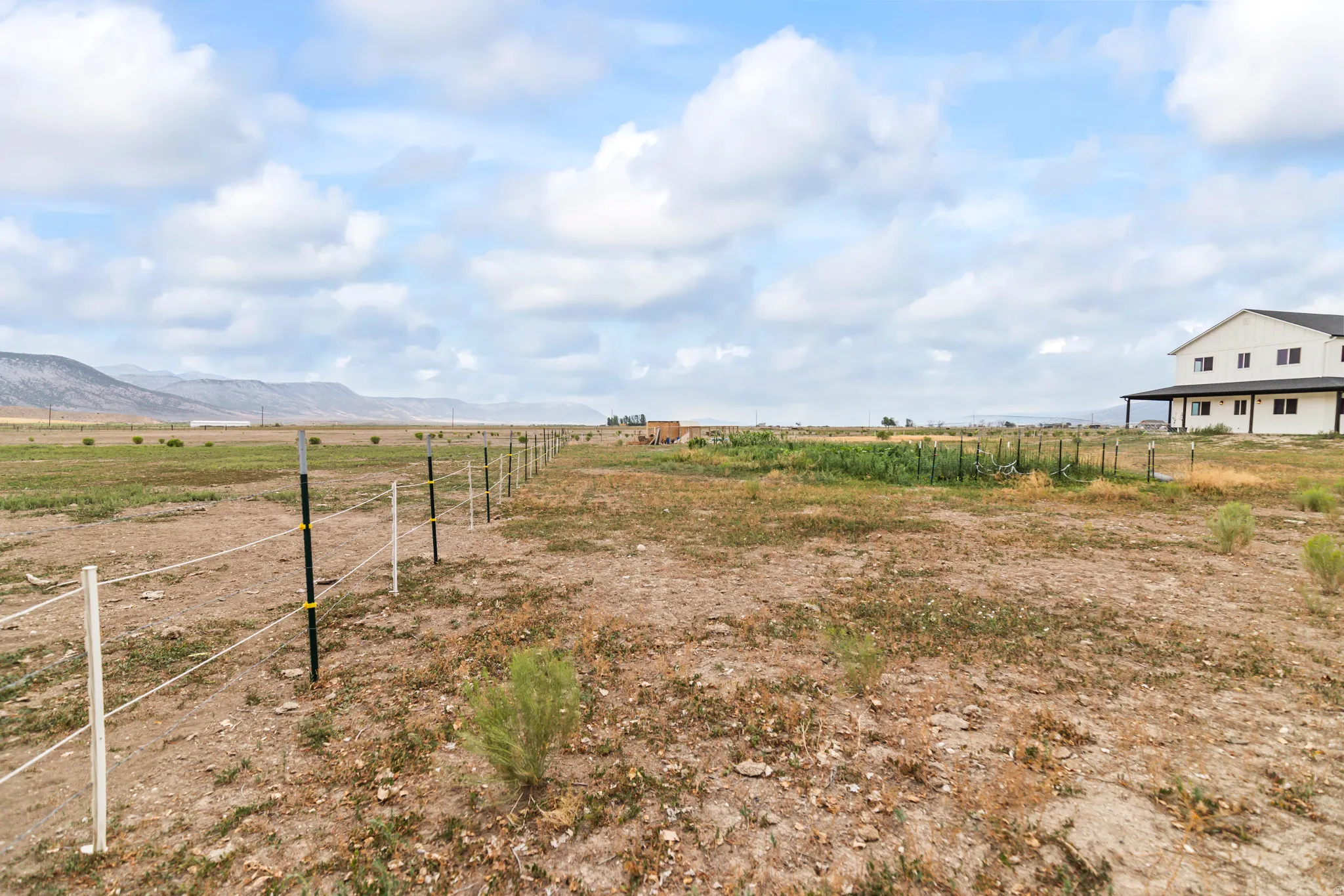 Expansive land with a partial wire fence, a dedicated garden area, and a large dwelling featuring a covered porch