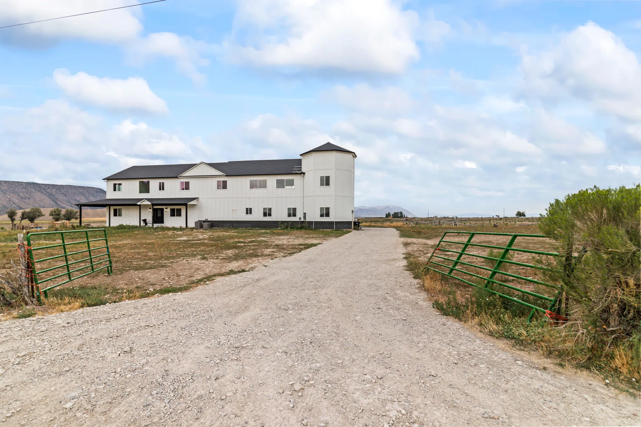 Gravel drive leading to a white multi-story structure with a covered entry, dark roof, and a cylindrical architectural element