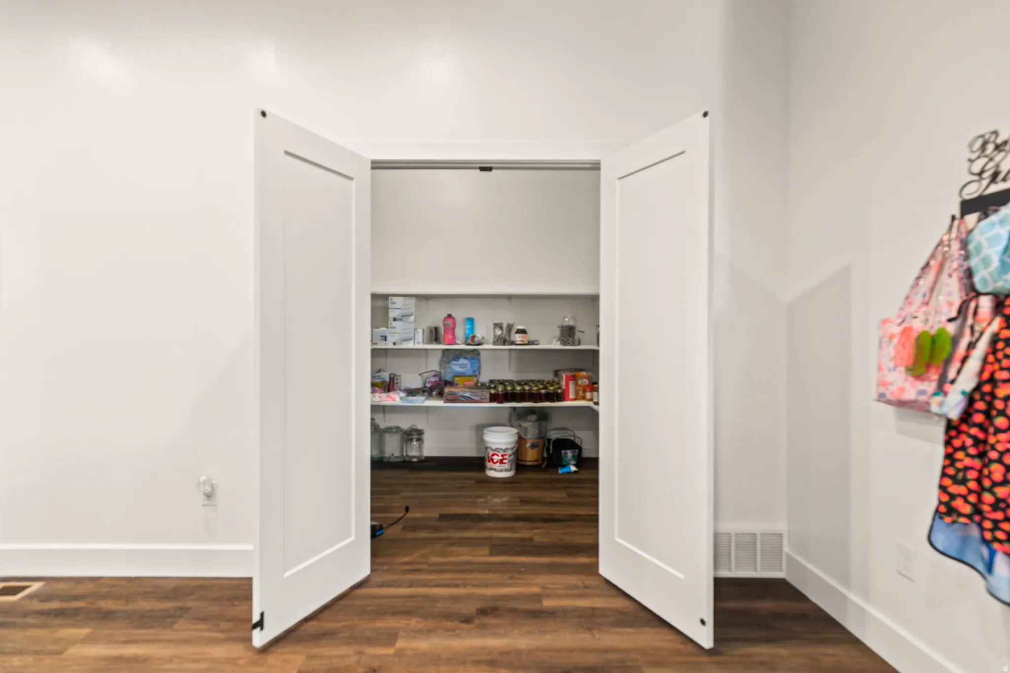 Pantry with multiple shelves, wood-finish flooring, and white bifold doors