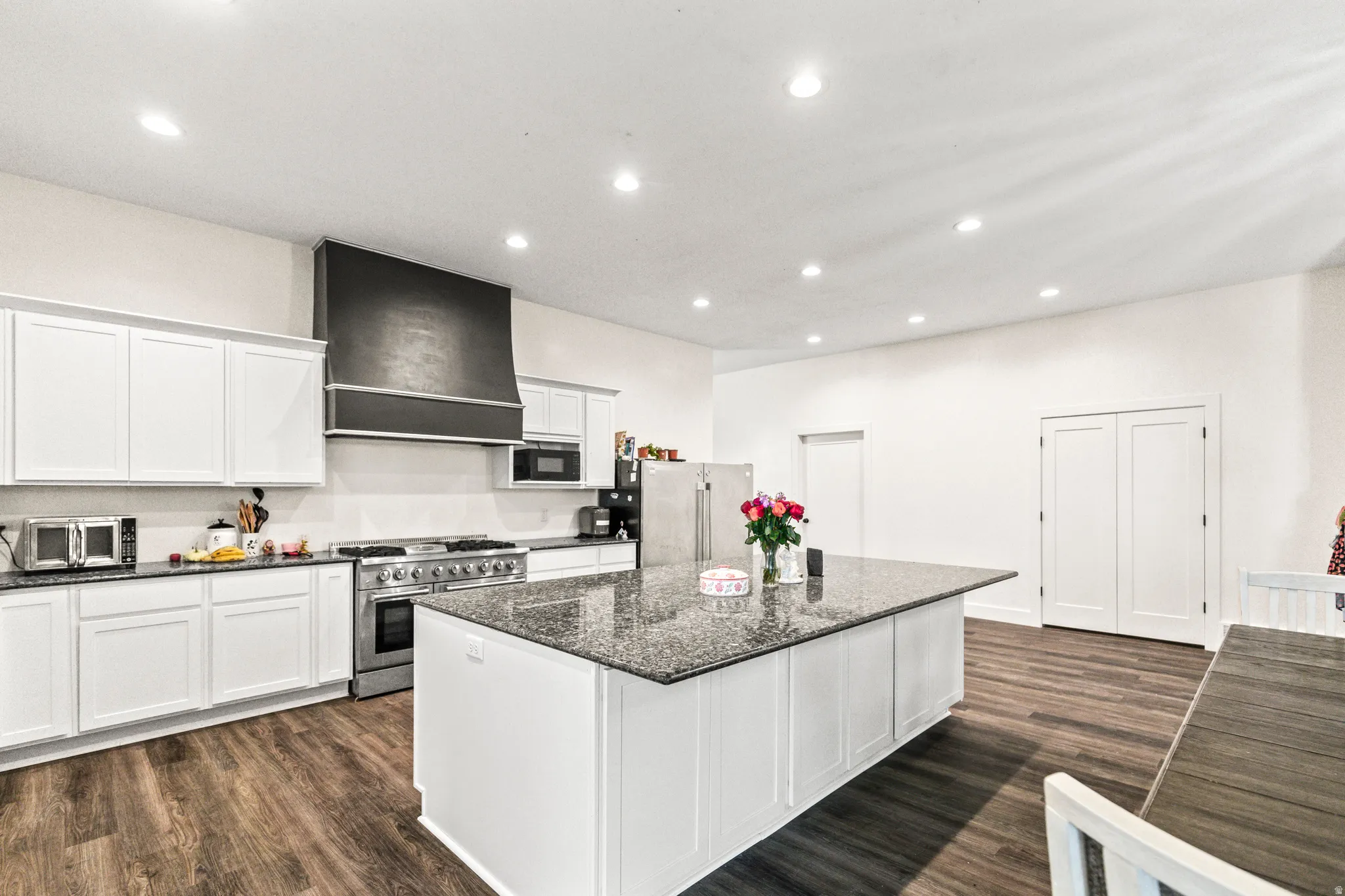 Kitchen featuring white cabinetry, a large kitchen island with a dark speckled countertop, stainless steel appliances, and wood-finish flooring