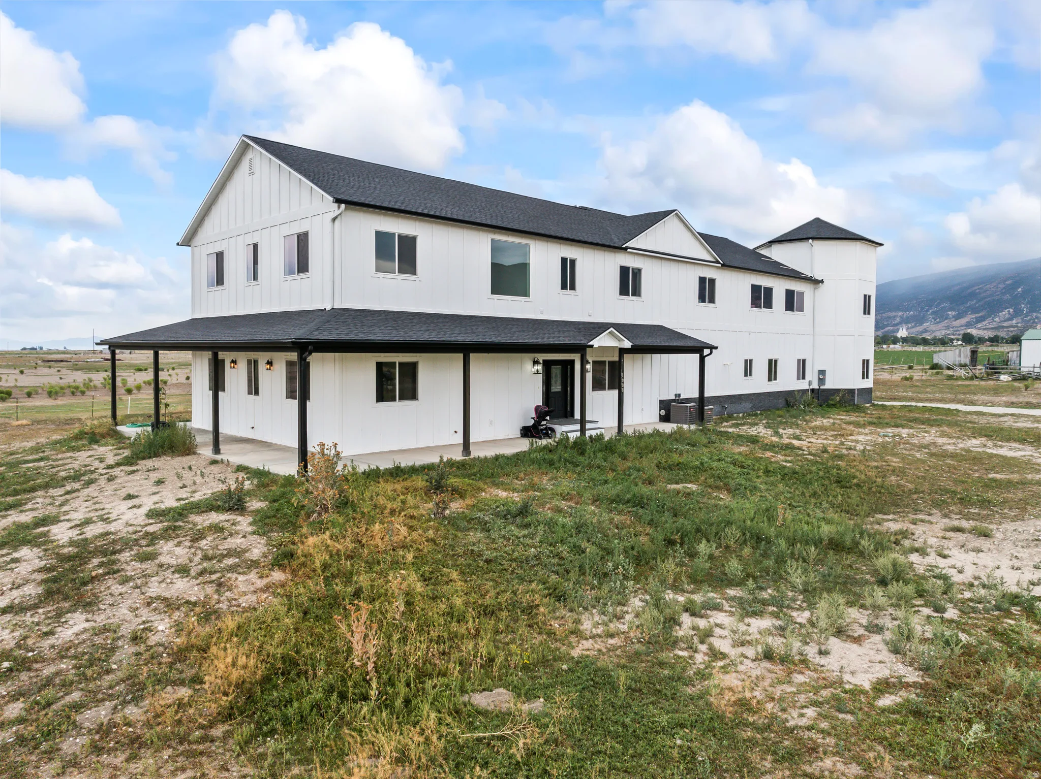 Modern farmhouse architecture featuring white board and batten siding, a black asphalt shingle roof, and a full-length covered porch with black support columns