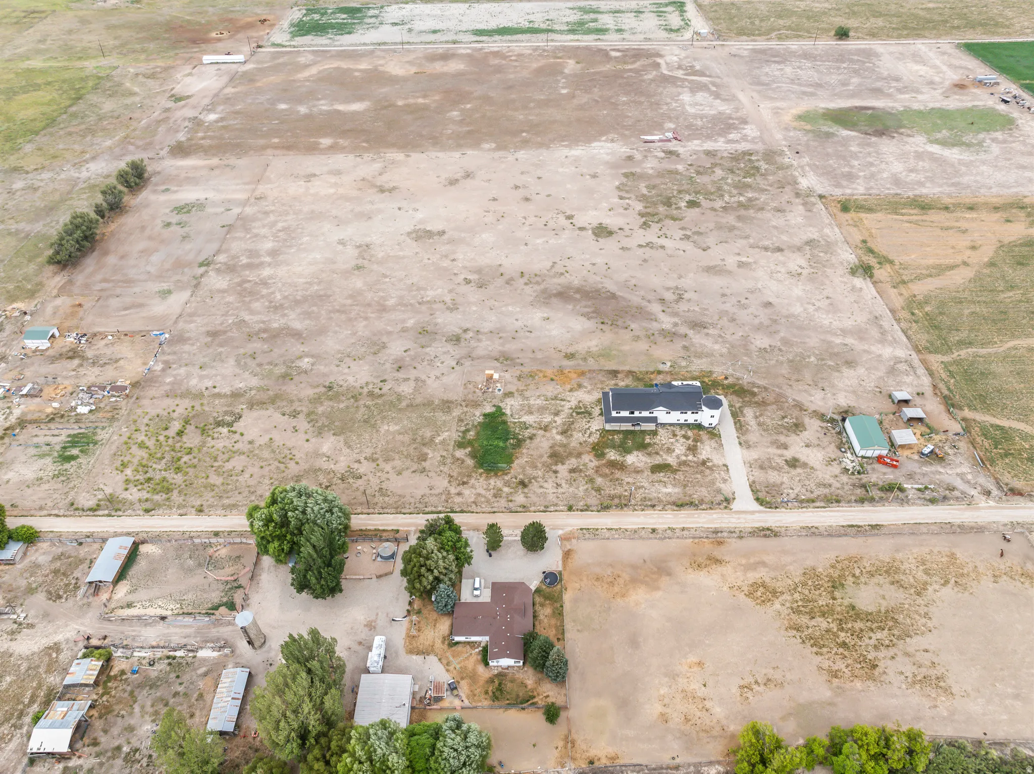 Expansive parcel featuring a main residence with a concrete driveway, secondary structure with a light green roof, and several outbuildings