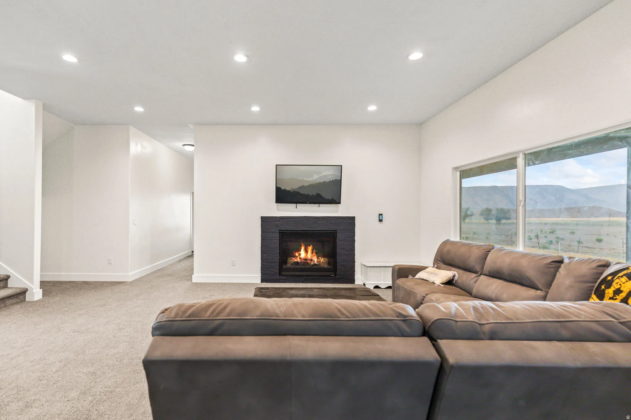 Spacious living area featuring a dark tile fireplace surround, large windows, recessed lighting, and light carpet flooring