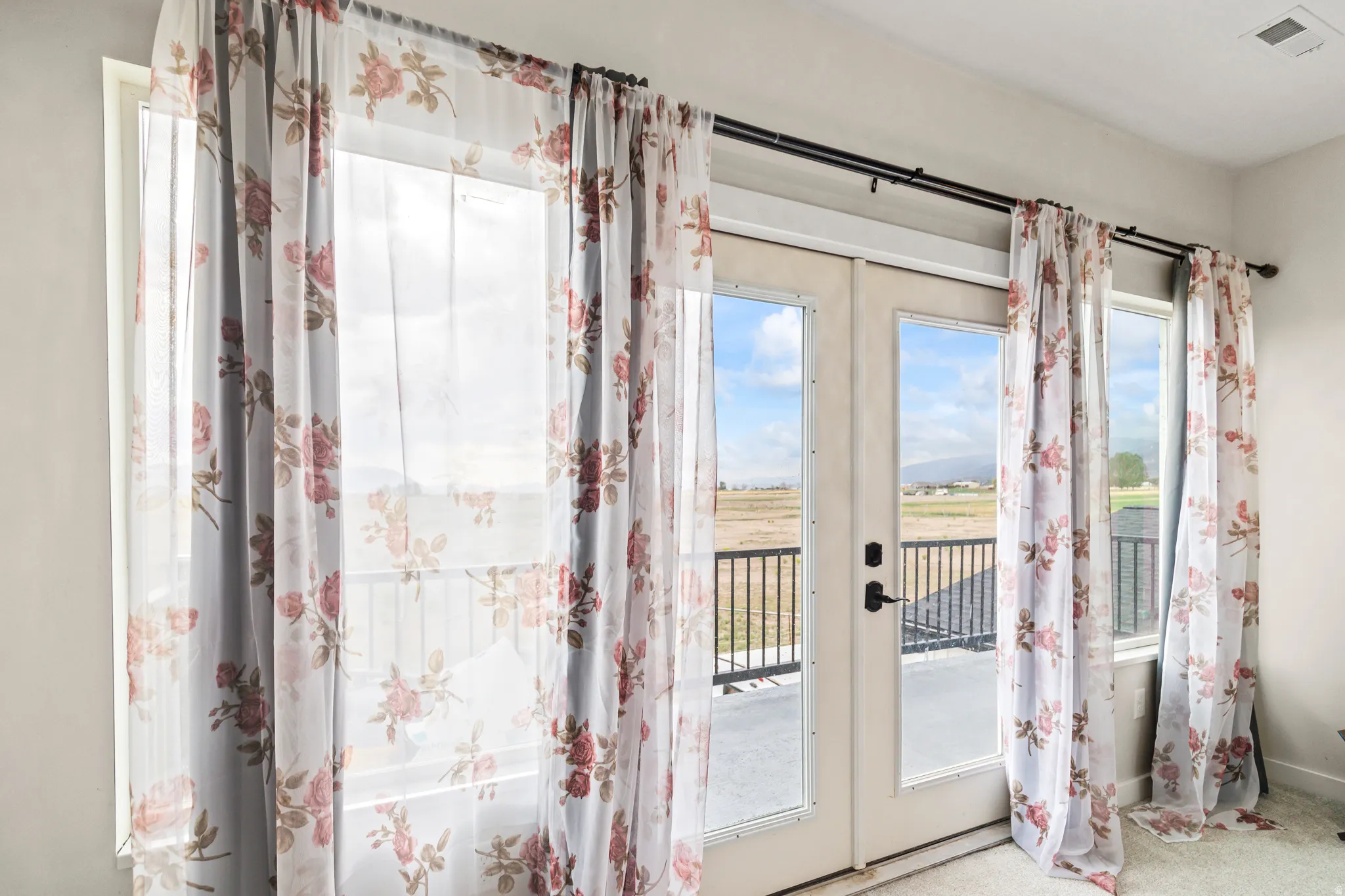 Double French doors with integrated glass panels, flanked by two fixed windows, provide access to an exterior balcony with a black metal railing