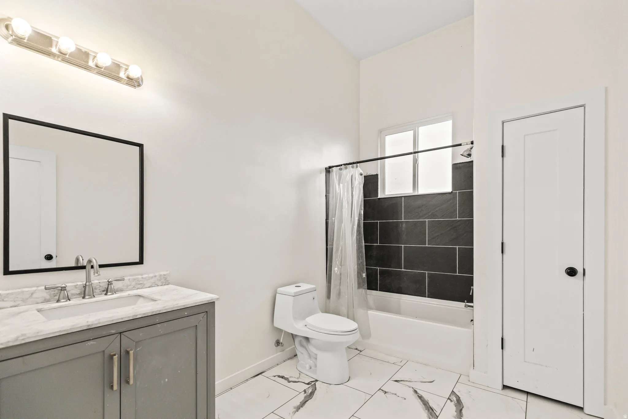Bathroom featuring a gray vanity with an undermount sink, a framed mirror, a five-bulb vanity light, and a tiled shower with a window