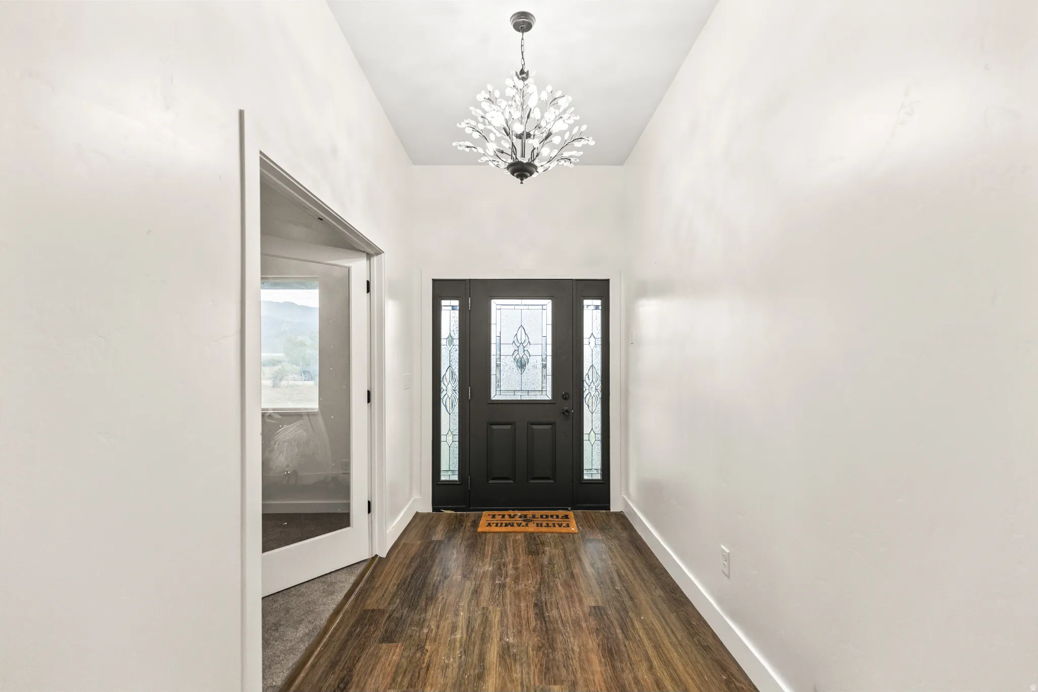 Entryway featuring wood-finish flooring, a decorative pendant light fixture, and a dark-paneled door with sidelight window details