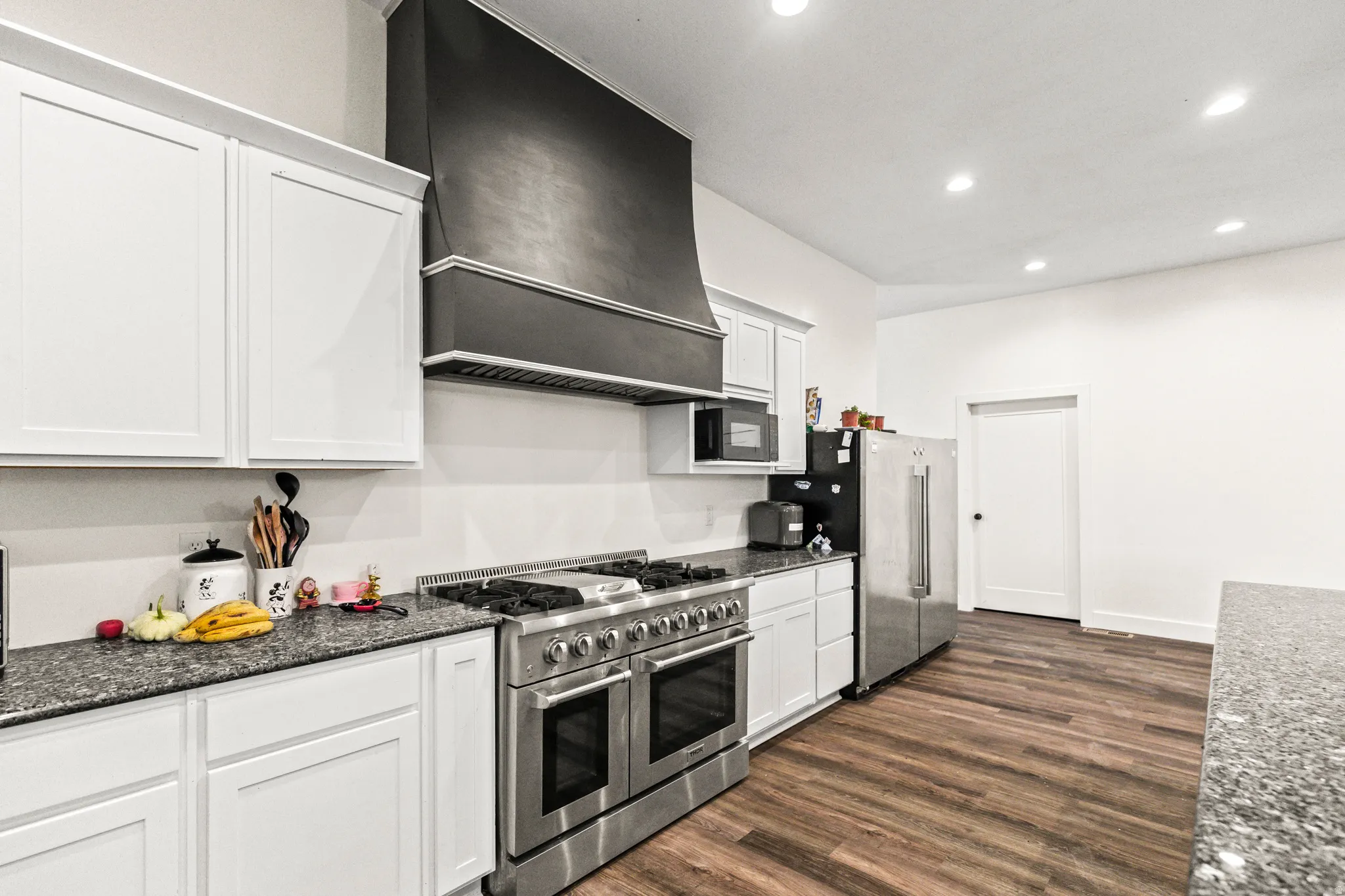 White cabinetry, stainless steel double oven range, dark gray range hood, wood-finish flooring, and recessed lighting