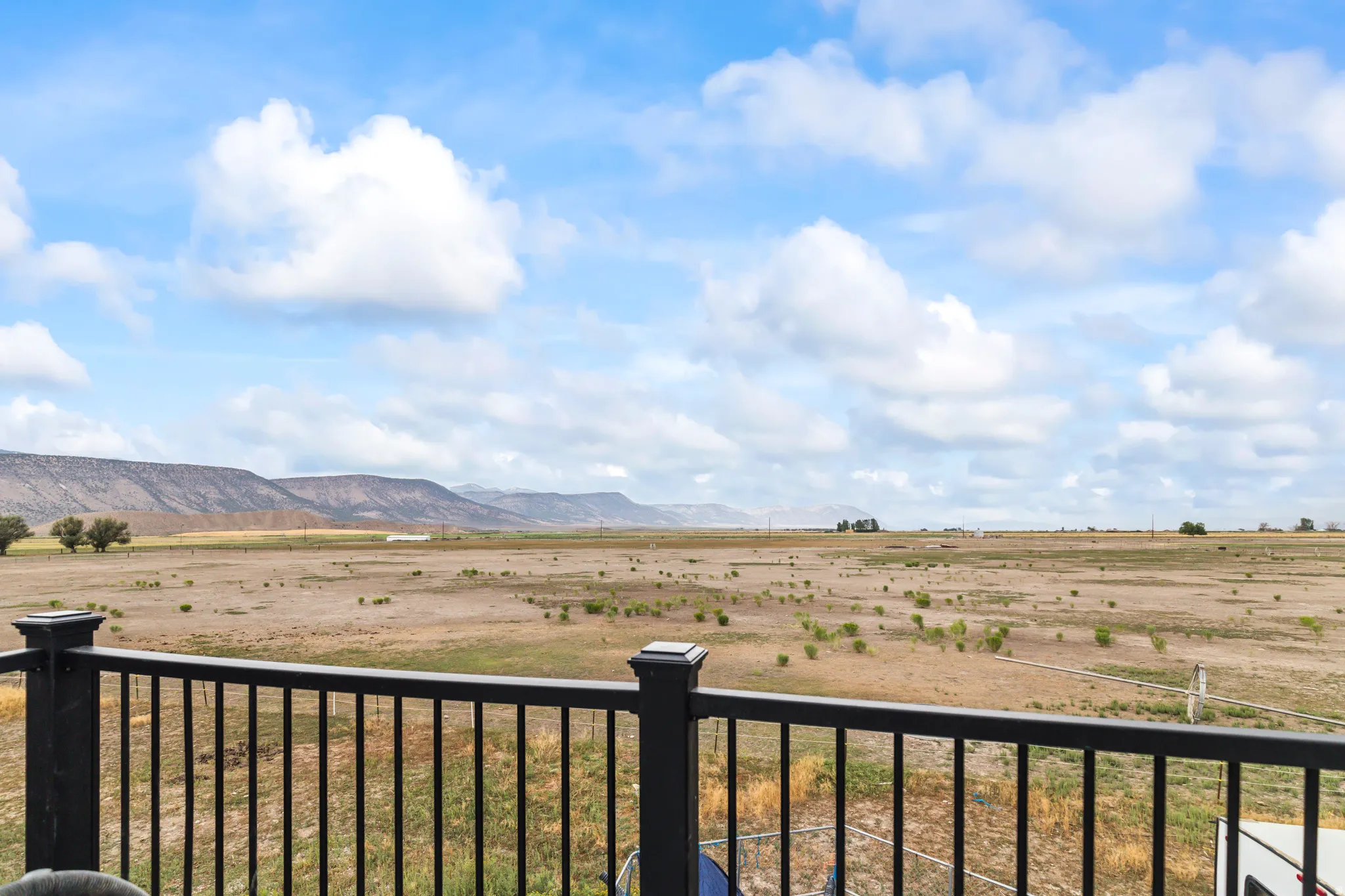 Expansive open landscape with distant mountains, black metal deck railing, and open sky