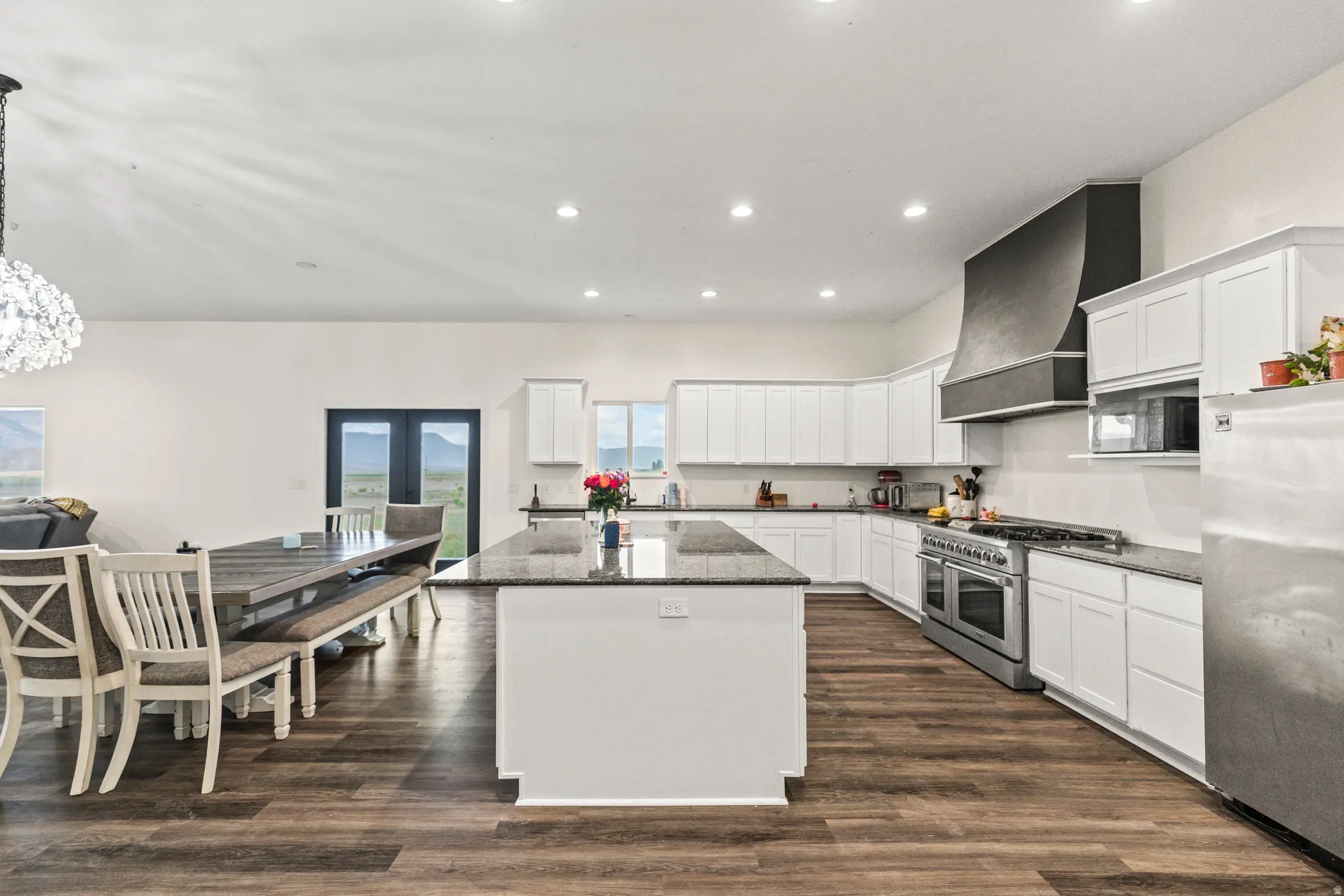 Open-concept kitchen and dining area featuring wood-finish flooring, white cabinetry, a large kitchen island with a stone countertop, and stainless steel appliances