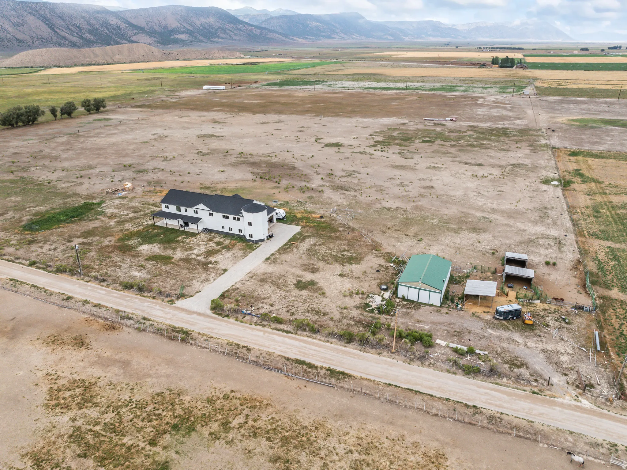 Expansive property featuring a multi-level residence with a cylindrical turret, a large green outbuilding, multiple open-sided shelters, and a gravel driveway