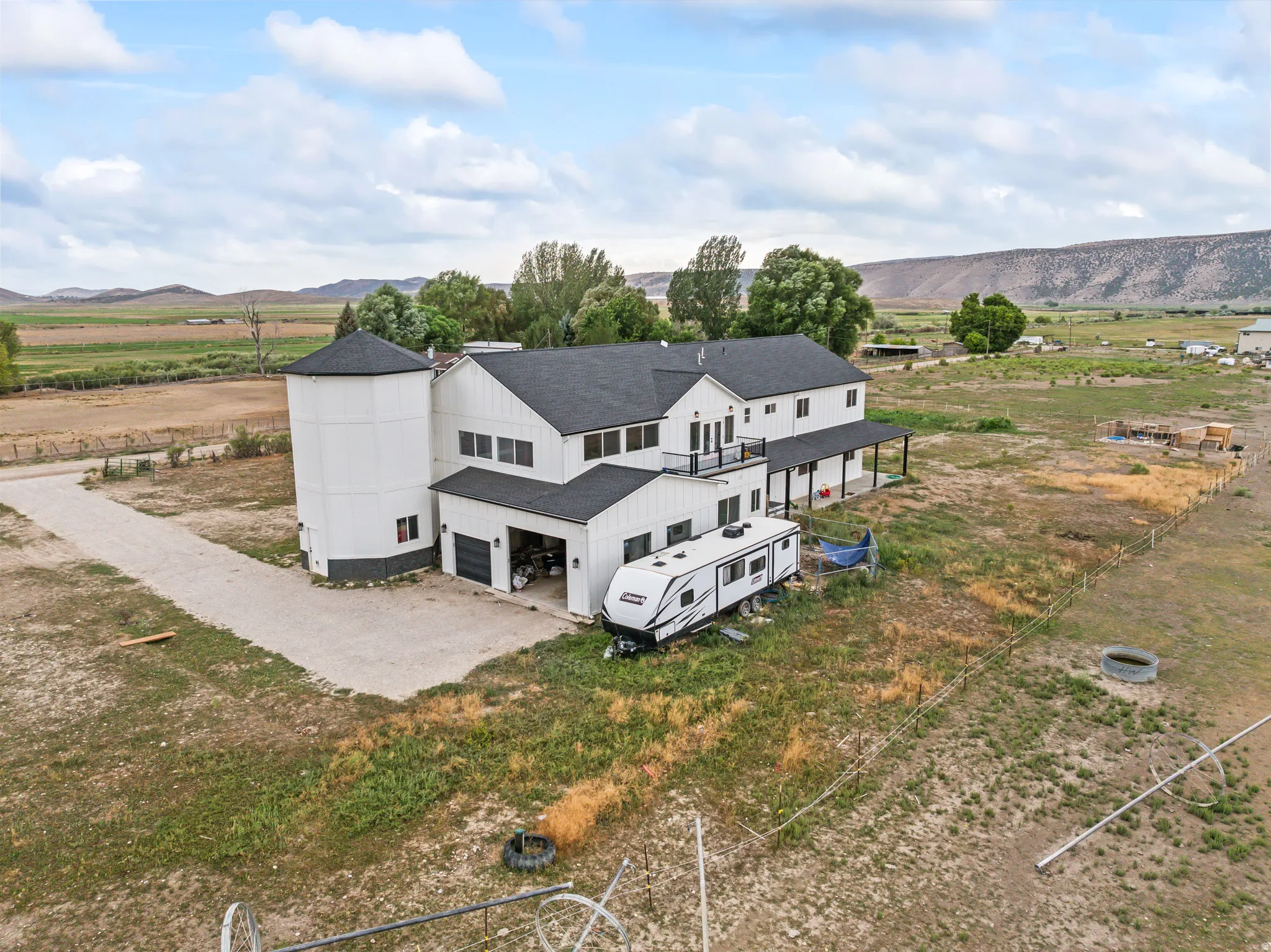 Modern farmhouse residence featuring a unique silo-style architectural element, a covered porch, a second-story balcony, and an attached garage