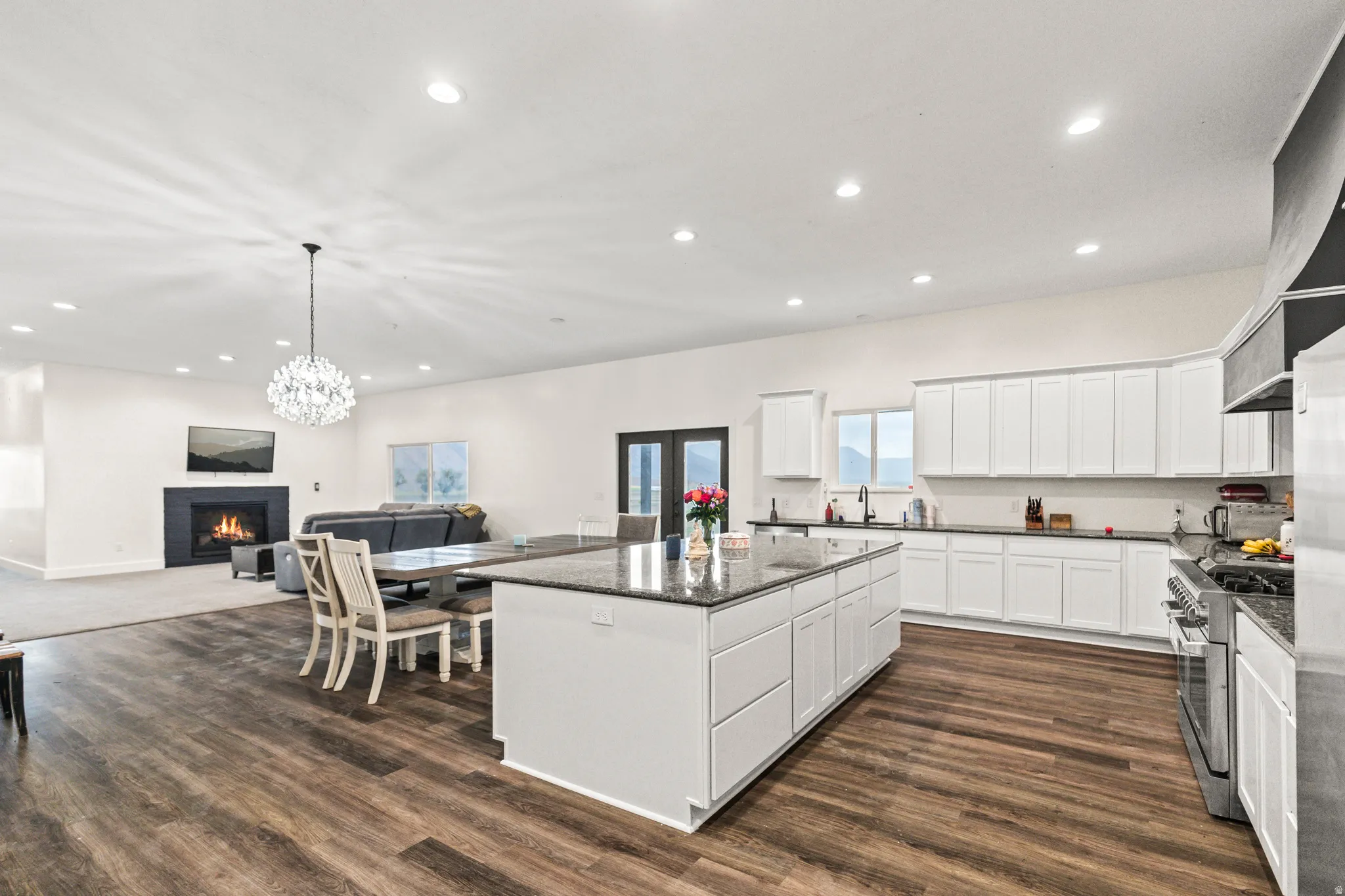 Expansive open-concept living area featuring a kitchen island with seating, dark wood-finish flooring, a contemporary chandelier, a built-in fireplace, and recessed lighting