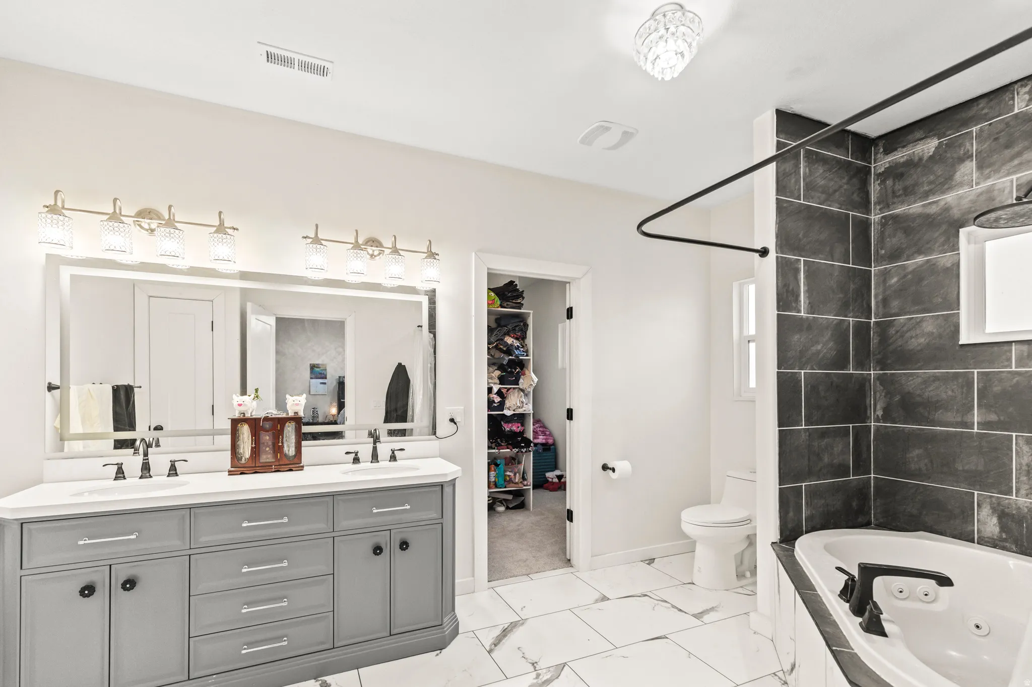 Dual vanity with gray cabinetry, white countertop, and expansive mirror with integrated lighting