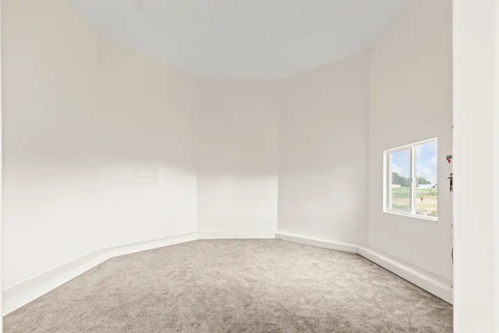 Curved architectural wall, window with exterior exposure, textured carpeting, white baseboards, and neutral wall tones