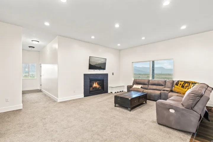 Recessed ceiling lighting, tiled fireplace surround, integrated wall-mounted television, large windows, and neutral carpet