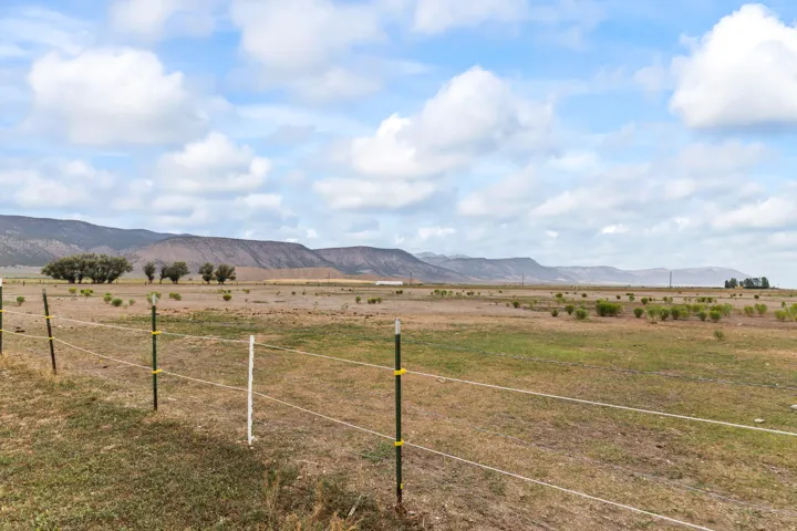 Expansive rural landscape featuring a distant mountain range, open fields with scattered vegetation, and a clear sky with clouds