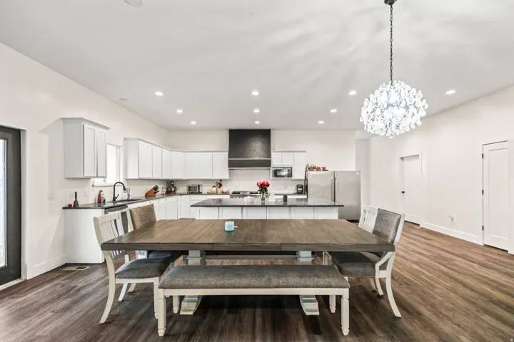 Open-concept kitchen and dining area featuring wood-finish flooring, white cabinetry, a kitchen island with dark countertops, a dark range hood, and a decorative chandelier