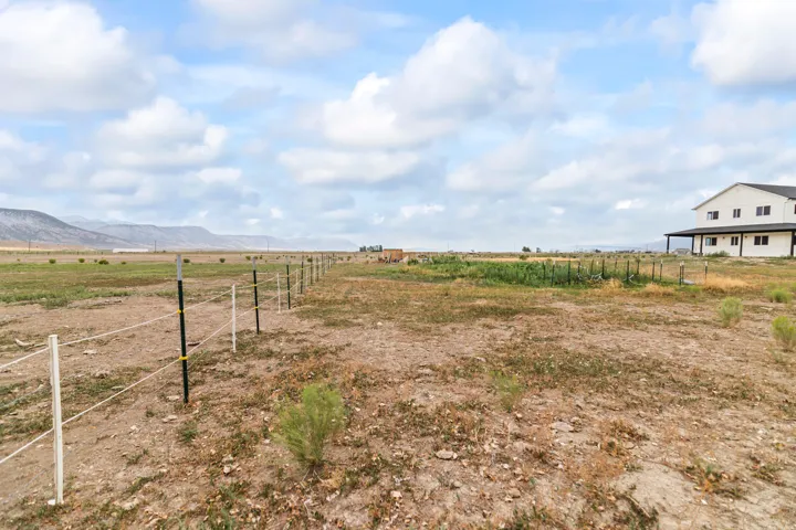 Expansive land with a partial wire fence, a dedicated garden area, and a large dwelling featuring a covered porch