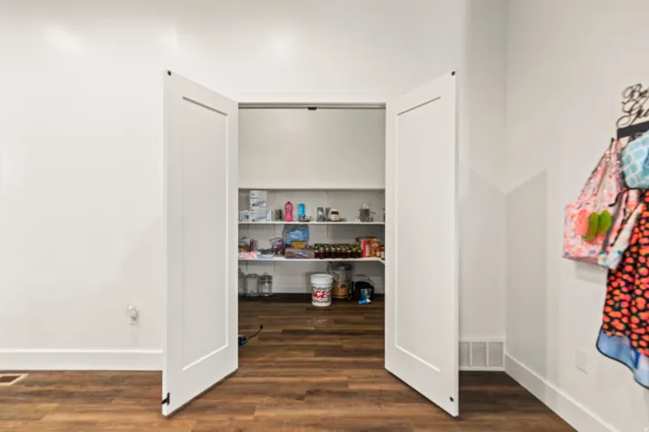 Pantry with multiple shelves, wood-finish flooring, and white bifold doors