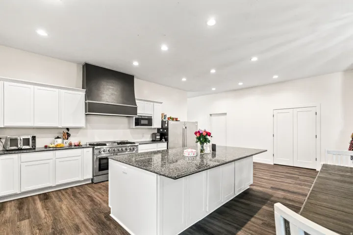 Kitchen featuring white cabinetry, a large kitchen island with a dark speckled countertop, stainless steel appliances, and wood-finish flooring