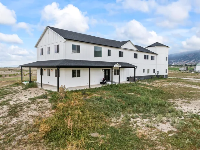 Modern farmhouse architecture featuring white board and batten siding, a black asphalt shingle roof, and a full-length covered porch with black support columns