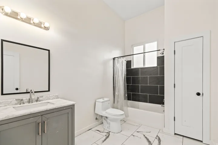 Bathroom featuring a gray vanity with an undermount sink, a framed mirror, a five-bulb vanity light, and a tiled shower with a window