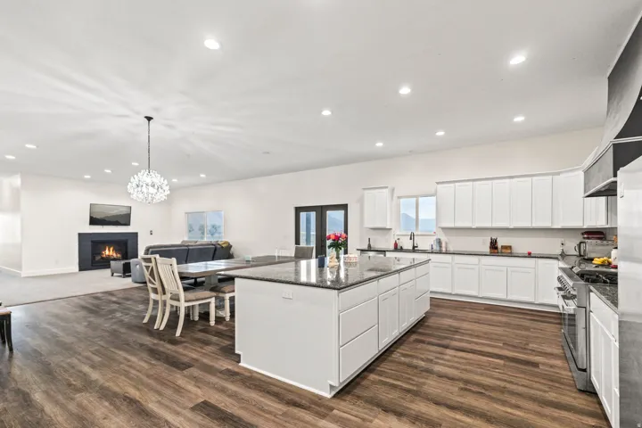 Expansive open-concept living area featuring a kitchen island with seating, dark wood-finish flooring, a contemporary chandelier, a built-in fireplace, and recessed lighting