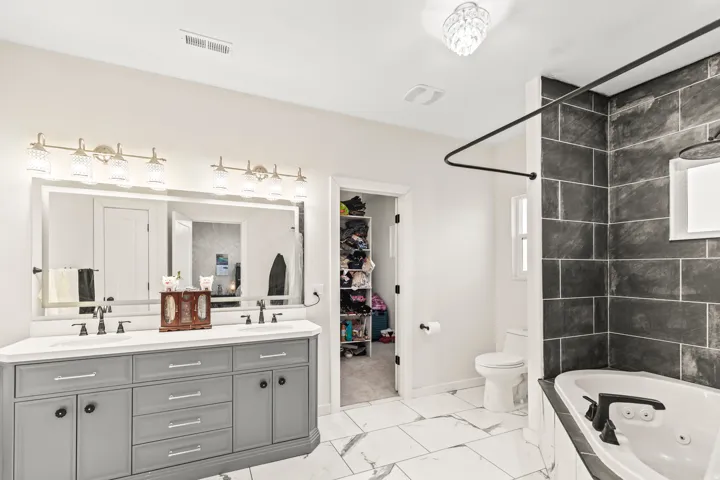 Dual vanity with gray cabinetry, white countertop, and expansive mirror with integrated lighting