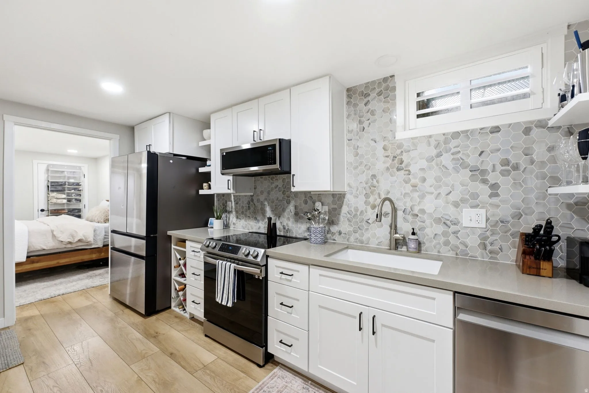 White shaker-style cabinetry, a hexagonal tile backsplash, stainless steel appliances, and wood-finish flooring