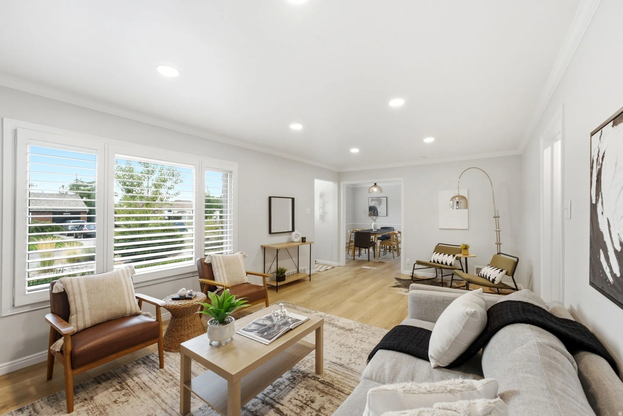 Bright, open-concept living space featuring recessed ceiling lighting, wood-finish flooring throughout, and expansive glass doors with horizontal shutters framing natural light