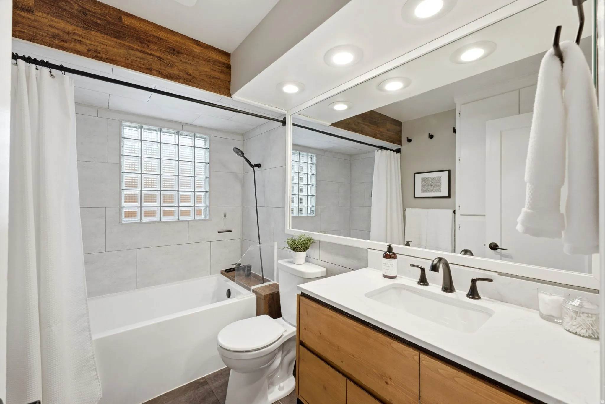 Spa-inspired primary bathroom featuring a wood-finish vanity with white quartz countertop, matte black fixtures, and an oversized framed mirror