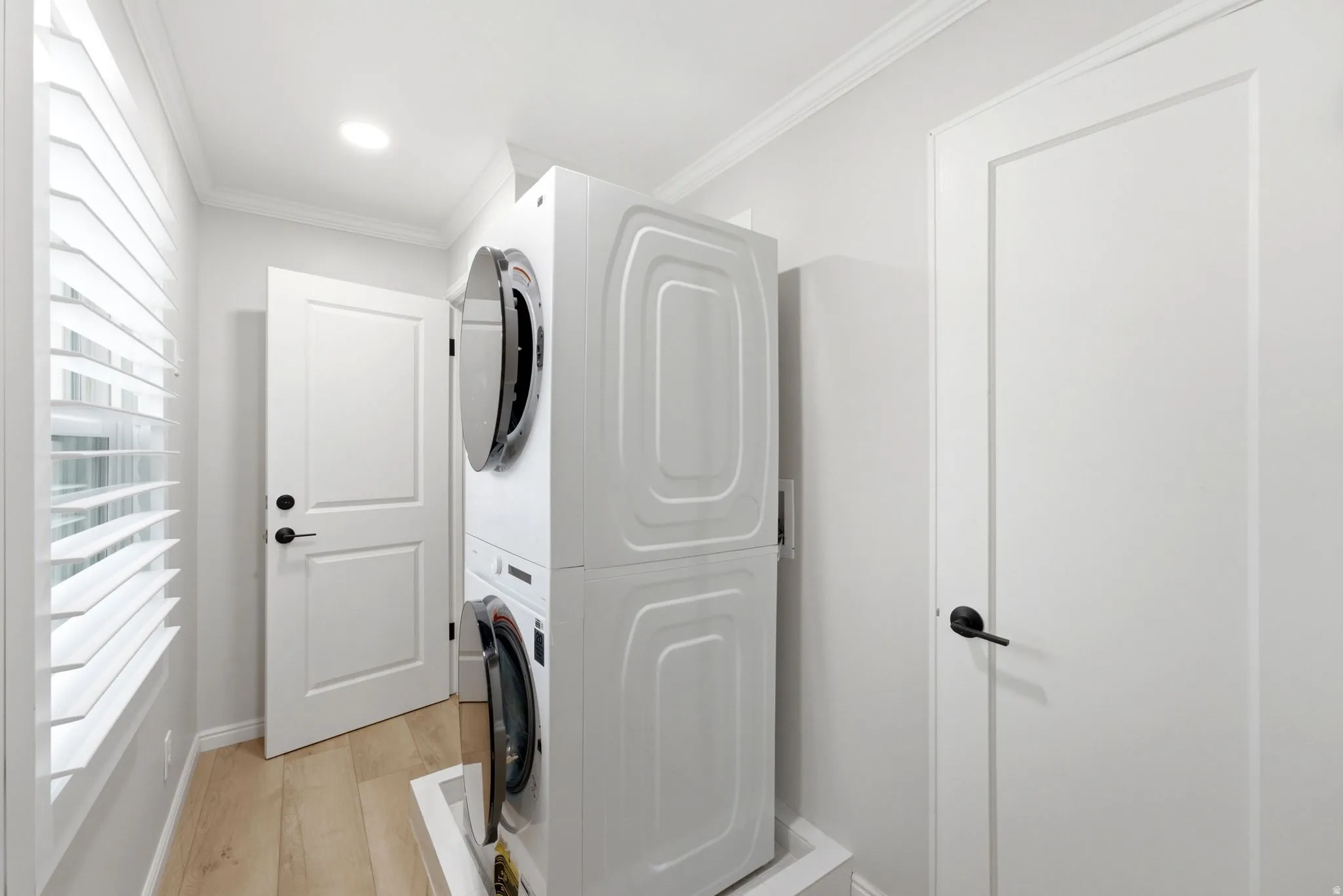Dedicated laundry area featuring a stacked washer and dryer, wood-finish flooring, plantation shutters, and recessed lighting
