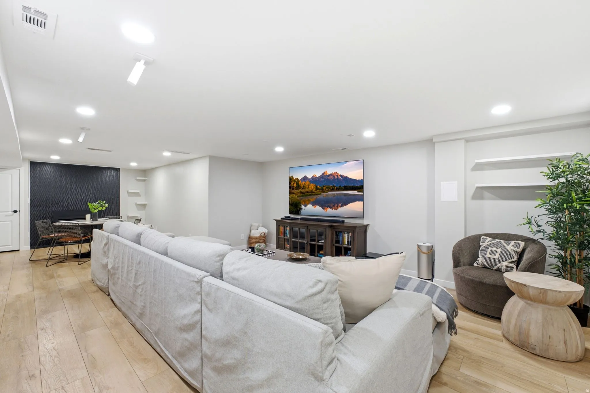 Open-concept living area featuring a light wood-finish plank floor, recessed ceiling lighting, and a gray upholstered sectional sofa