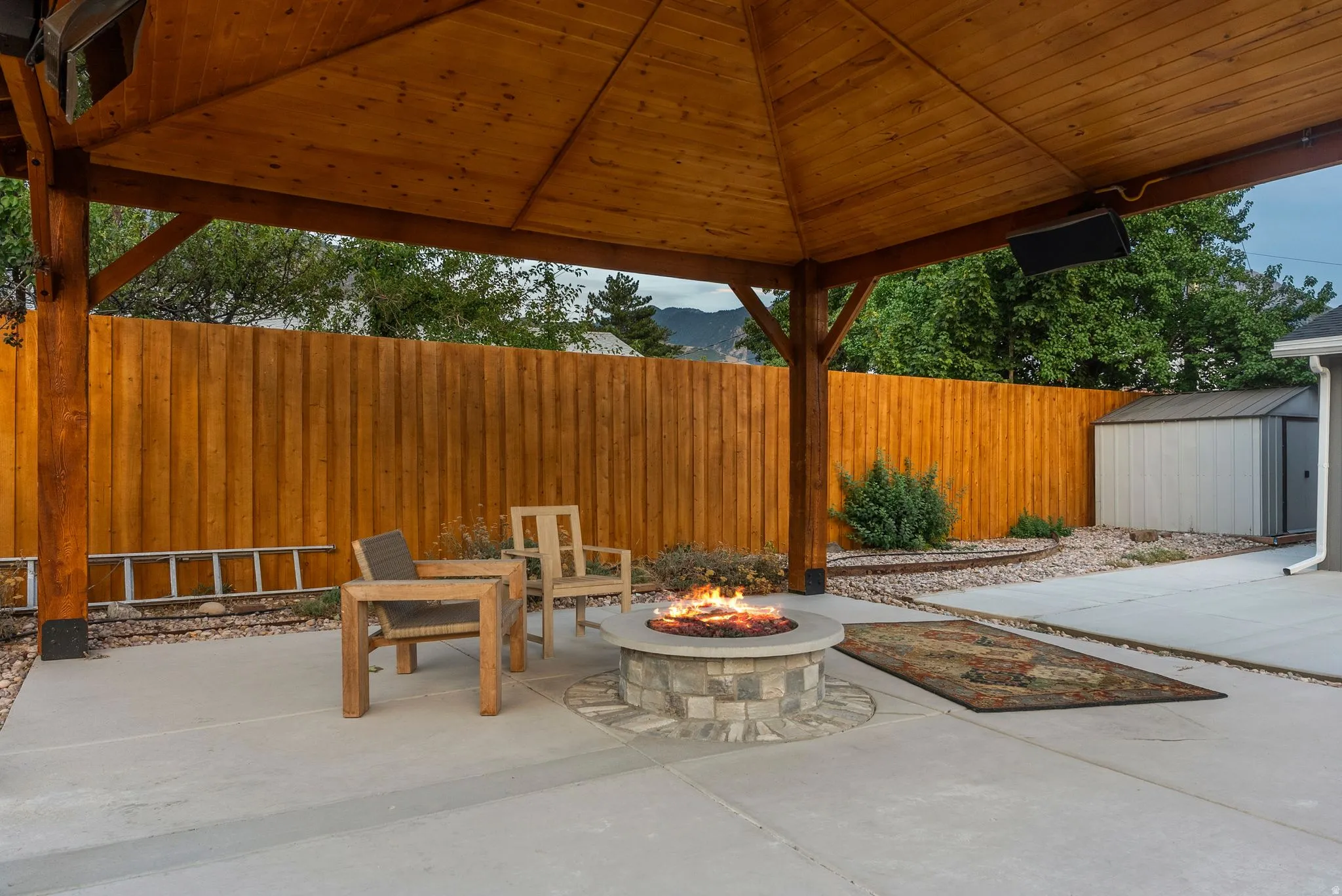 Expansive concrete patio with a wooden gazebo, built-in stone fire pit, and privacy fencing