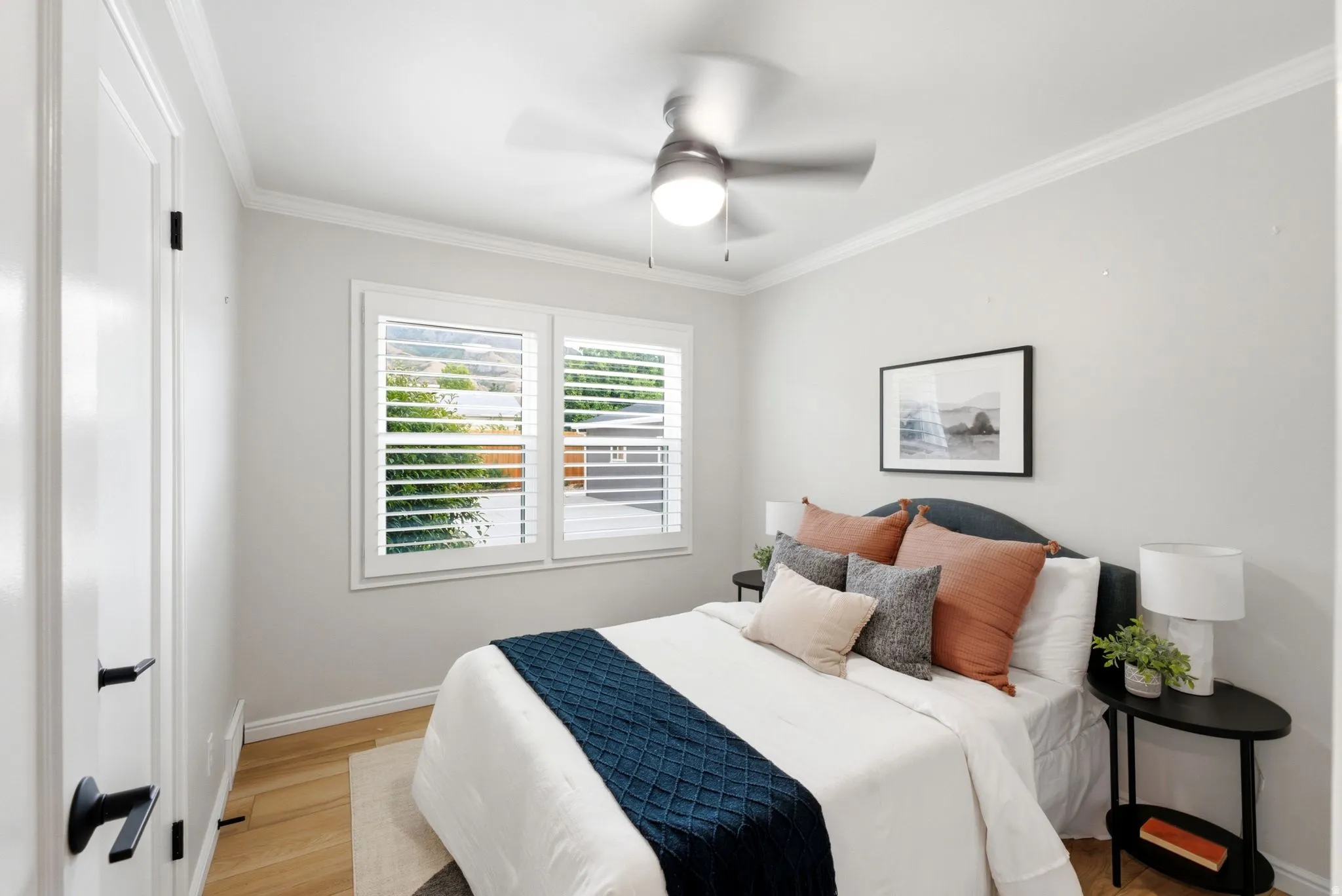 Bright bedroom featuring hardwood flooring, a ceiling fan with integrated lighting, and plantation shutters framing dual windows