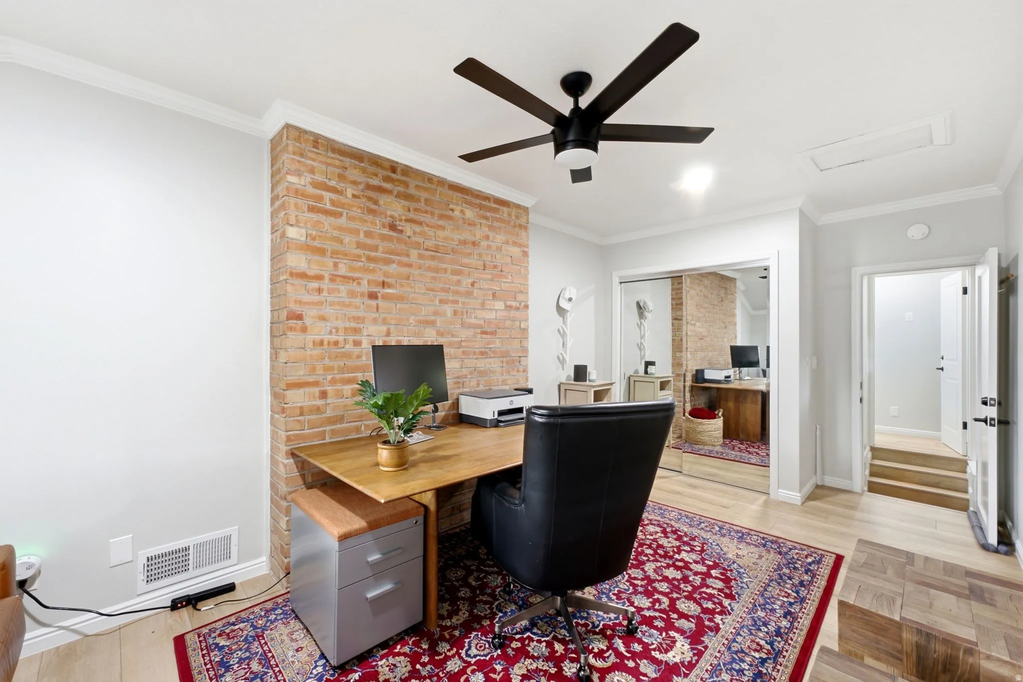 Exposed brick wall accent, wood-finish flooring, ceiling fan, crown molding, and mirrored closet doors