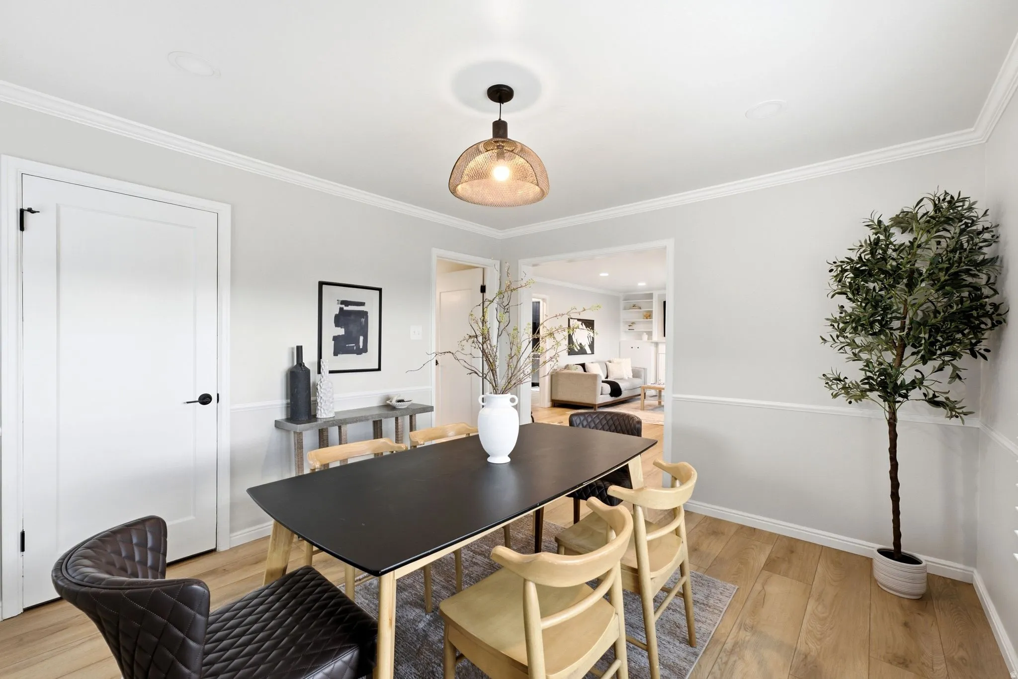 Dining space featuring a black wood-finish table, natural wood chairs with woven details, warm pendant lighting with an amber glass shade, and hardwood flooring throughout
