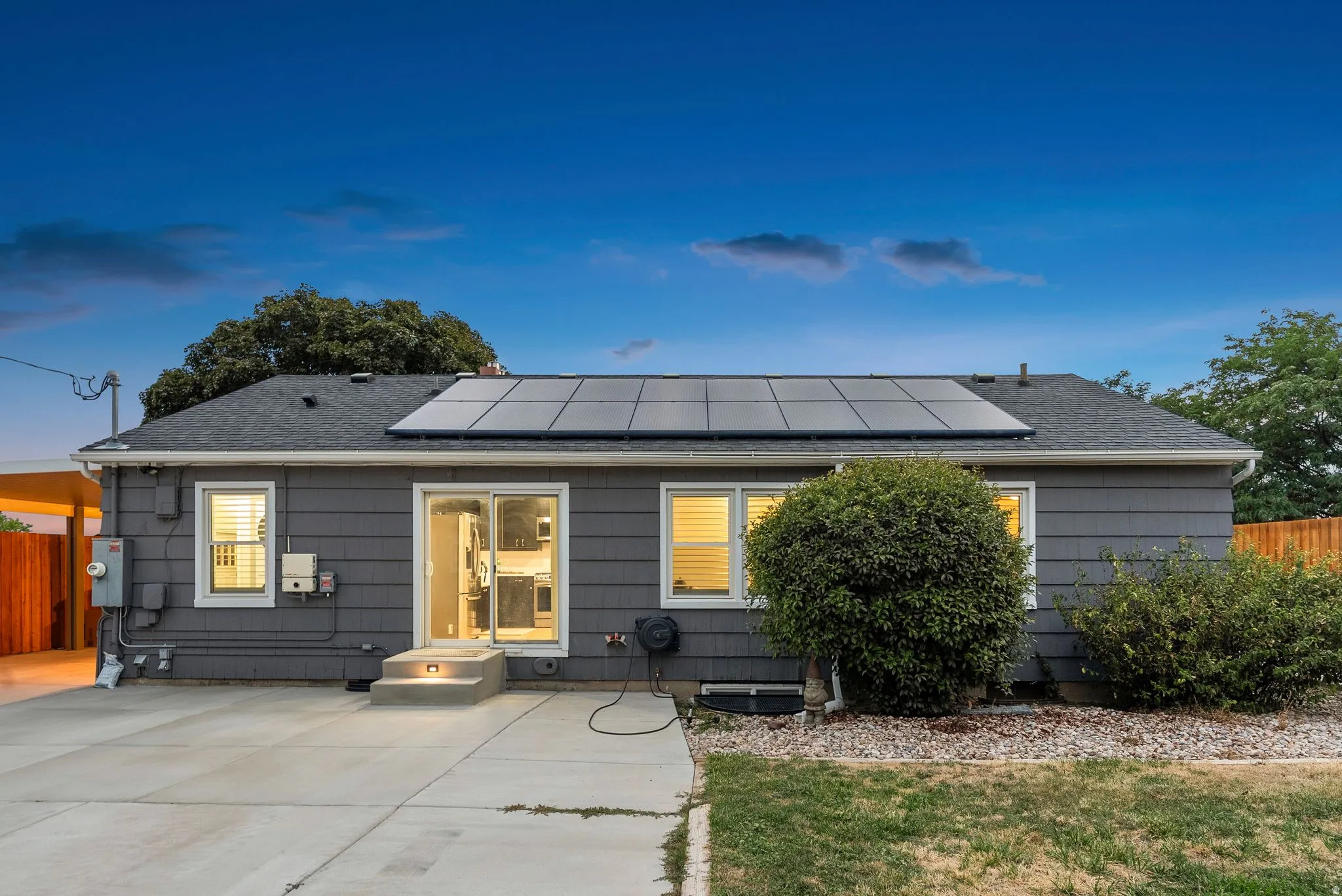 Dark gray siding with white trim, multi-panel solar array, concrete patio, two-step entryway, and sliding glass doors
