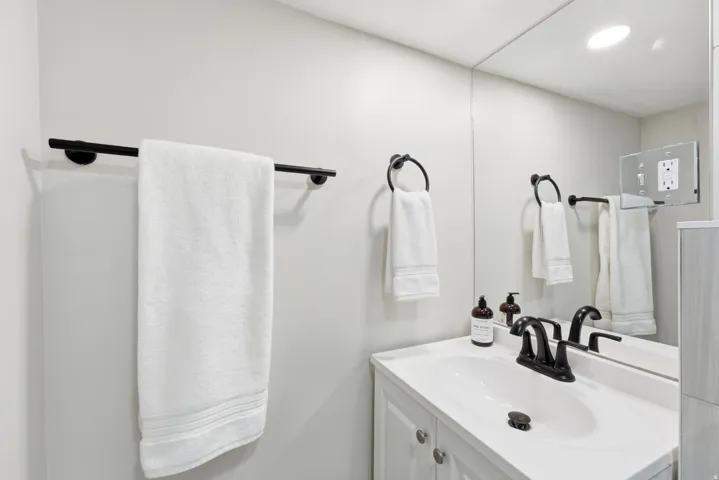 White vanity with a single basin sink, matte black faucet, and full-wall mirror
