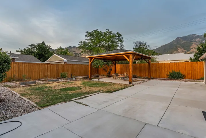 Spacious backyard featuring a concrete patio, a wooden pergola, a full privacy fence, and raised garden beds