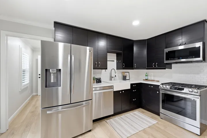 Modern kitchen featuring dark wood-finish cabinetry, stainless steel appliances, a farmhouse sink, subway tile backsplash, and light wood-finish flooring