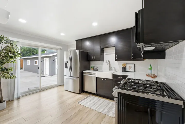 Modern kitchen featuring dark wood-finish cabinetry, stainless steel appliances, a farmhouse-style sink, and light wood-finish flooring