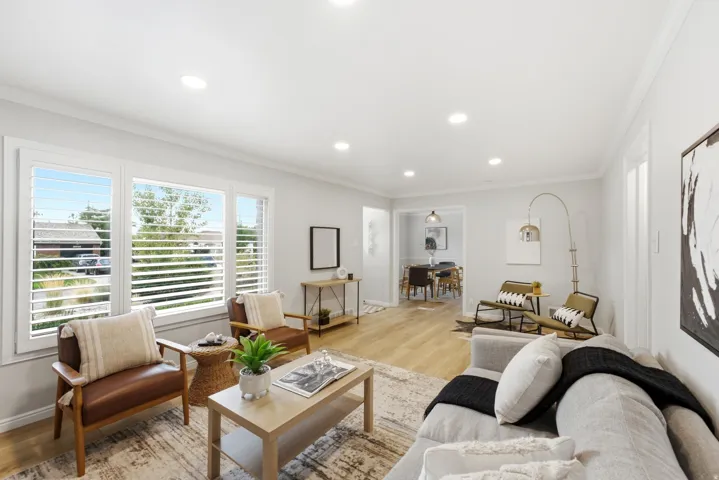 Bright, open-concept living space featuring recessed ceiling lighting, wood-finish flooring throughout, and expansive glass doors with horizontal shutters framing natural light