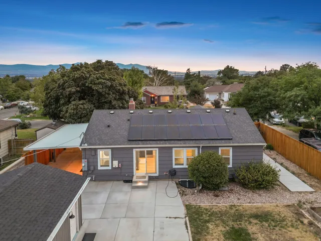 Gabled roofline with solar panels, rear concrete patio, sliding glass door, and a detached garage with a dark shingle roof